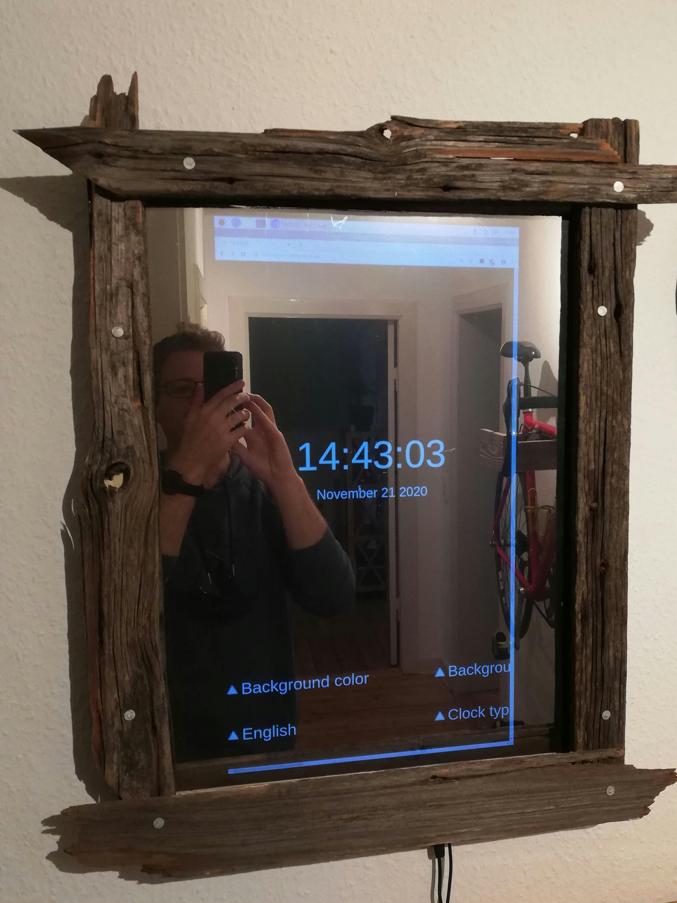 Halbtransparenter Spiegel durch den ein Bildschirm scheint, auf dem eine Uhr zu sehen ist